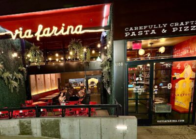 A closer shot of Via Farina from the outside at night, the orange pizza oven visible inside