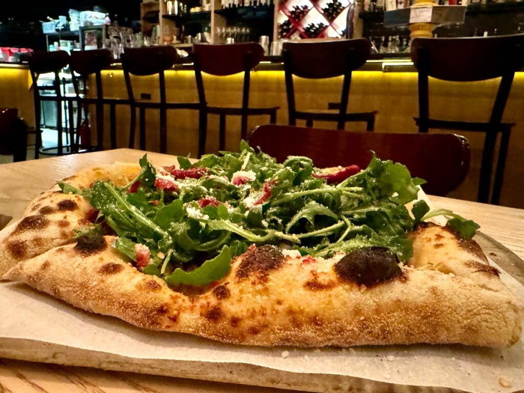 a pizza topped with arugula, sausage, roasted peppers, the salciccia