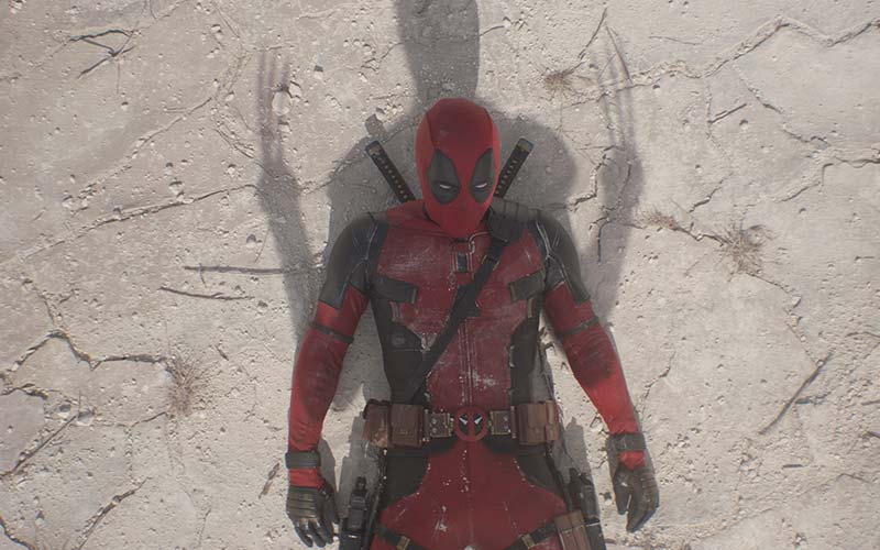 The shadow of Wolverine, claws out, stands over Deadpool laying on the snow