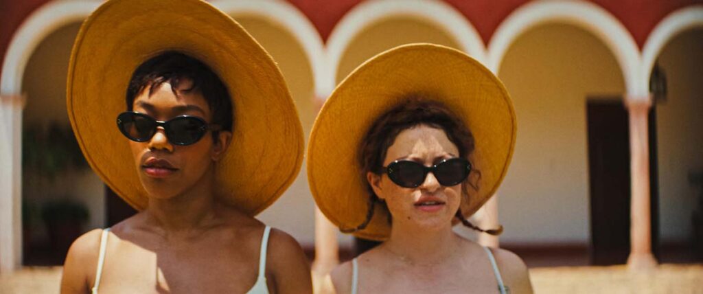 Naomi Ackie and Alia Shawat wearing sun hats overlooking the island pool