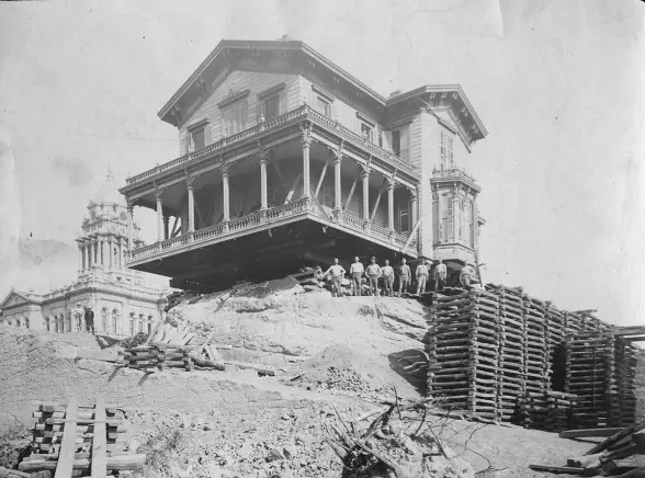 Photo of a house on Douglas Street being raised so the ground underneath could be cut away and the house lowered