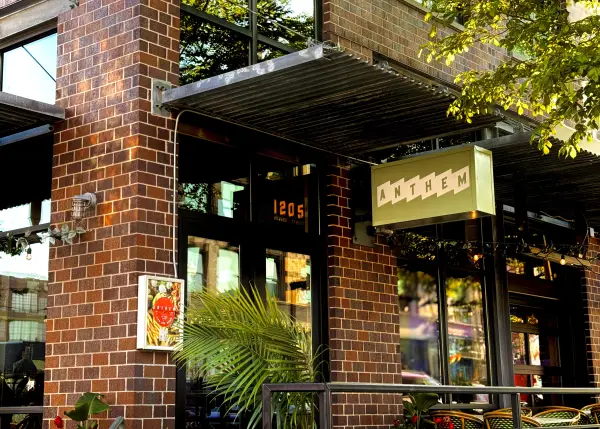 Anthem’s green sign hangs outside the restaurant’s Old Market entrance with patio seating and leafy plants in view.